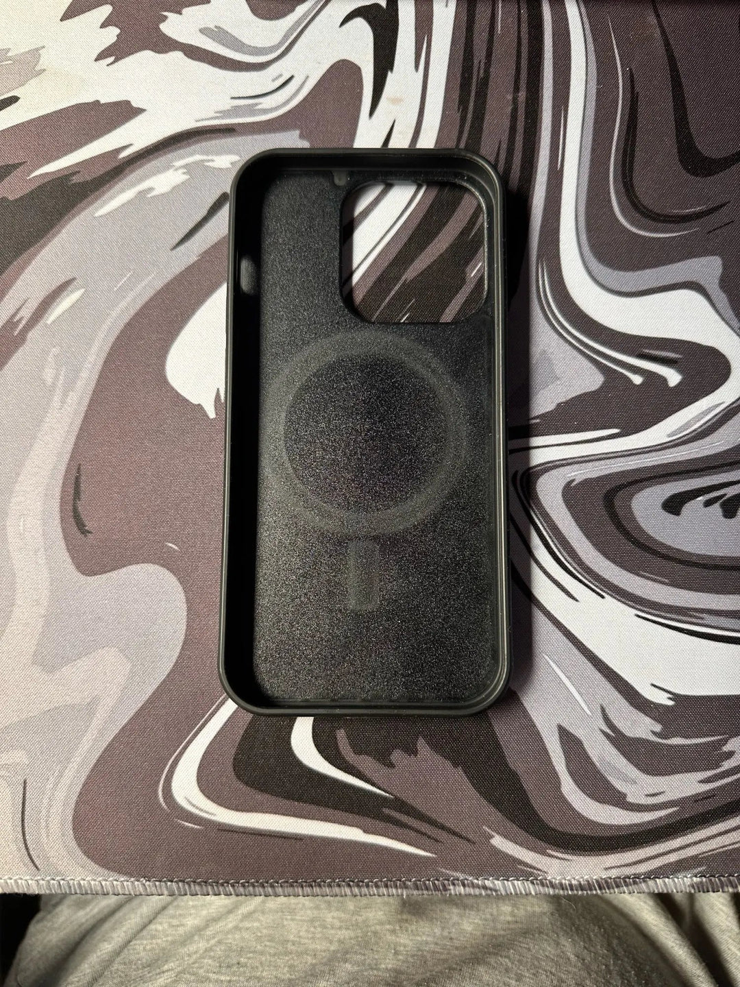 The Carbon Fiber for iPhone, a sleek black case with a circular design on the inside, rests elegantly on a black and white marbled surface, offering superior protection.