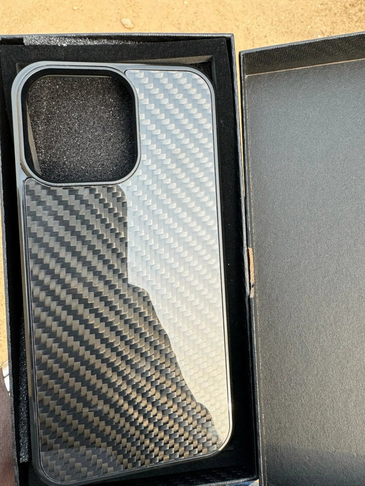 A sleek Carbon Fiber for iPhone phone case inside an open black box on a light-colored surface, offering unparalleled protection.