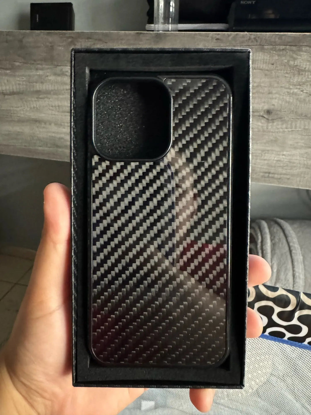 A hand holding the sleek new Carbon Fiber for iPhone case inside a black packaging box, designed for top-tier iPhone protection.