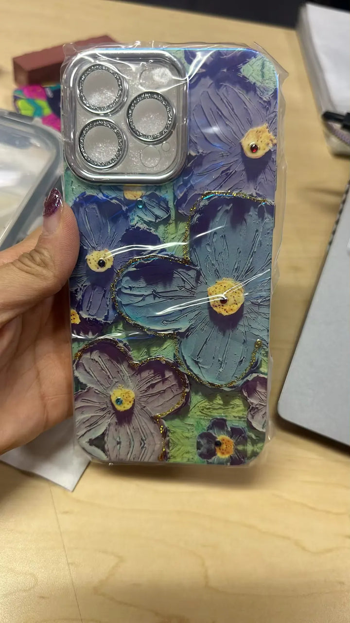 A photo of a phone case with a 3D floral design. The flowers are painted in pastel colors and adorned with glitter and rhinestones. The case is being held in someone's hand.