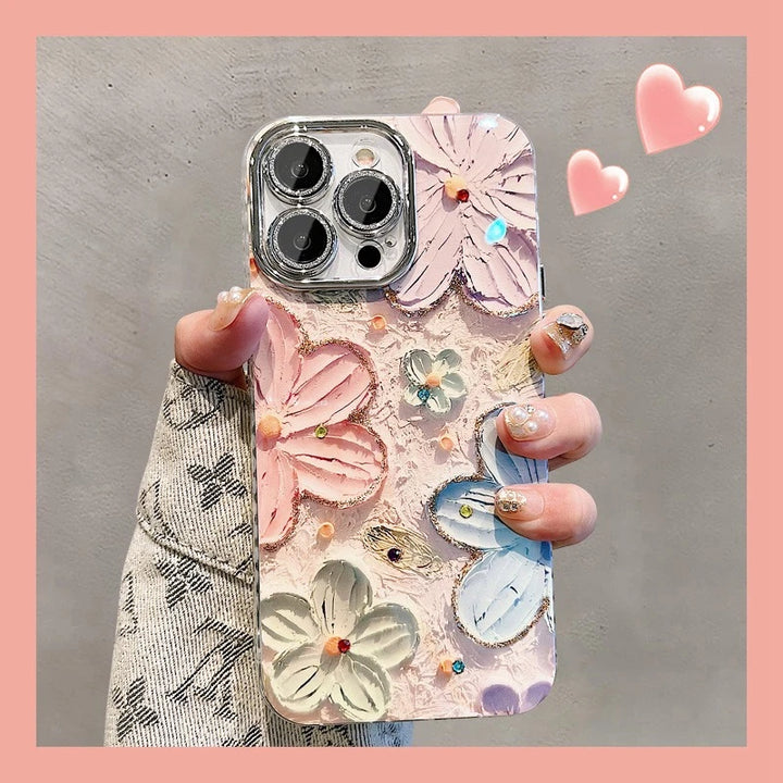 A photo of a phone case with a 3D floral design. The flowers are painted in pastel colors and adorned with glitter and rhinestones. The case is being held in someone's hand.