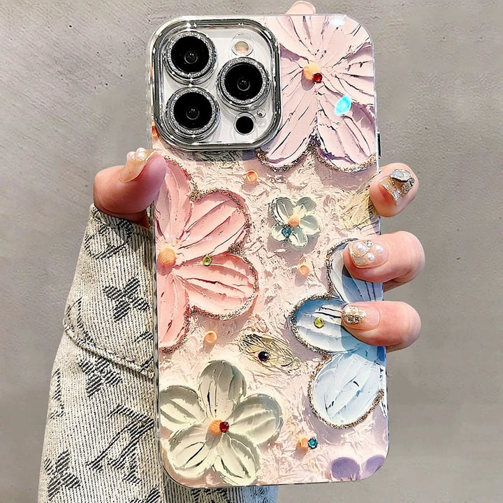 A photo of a phone case with a 3D floral design. The flowers are painted in pastel colors and adorned with glitter and rhinestones. The case is being held in someone's hand.