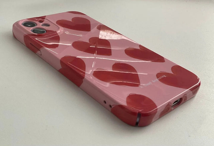 The Couple Hearts for iPhone acrylic case, featuring playful heart patterns on a pink background, is placed on a light grey surface.