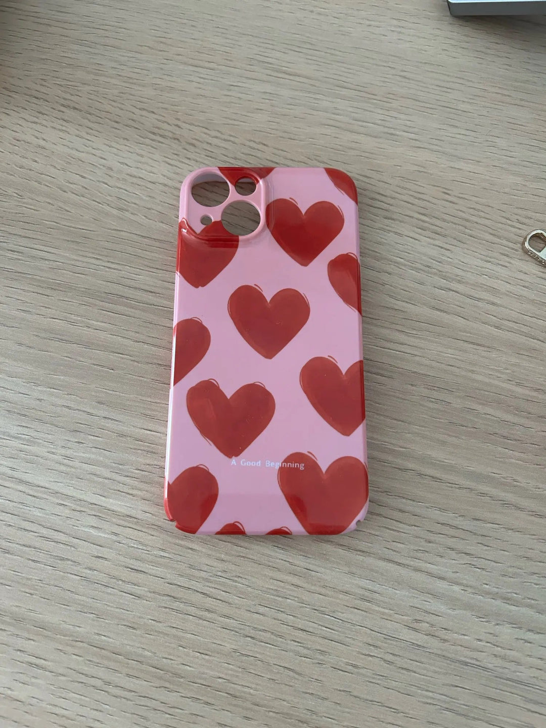 A Couple Hearts for iPhone - Acrylic case, featuring a pink color with a playful heart pattern design, is placed on a light wooden surface.