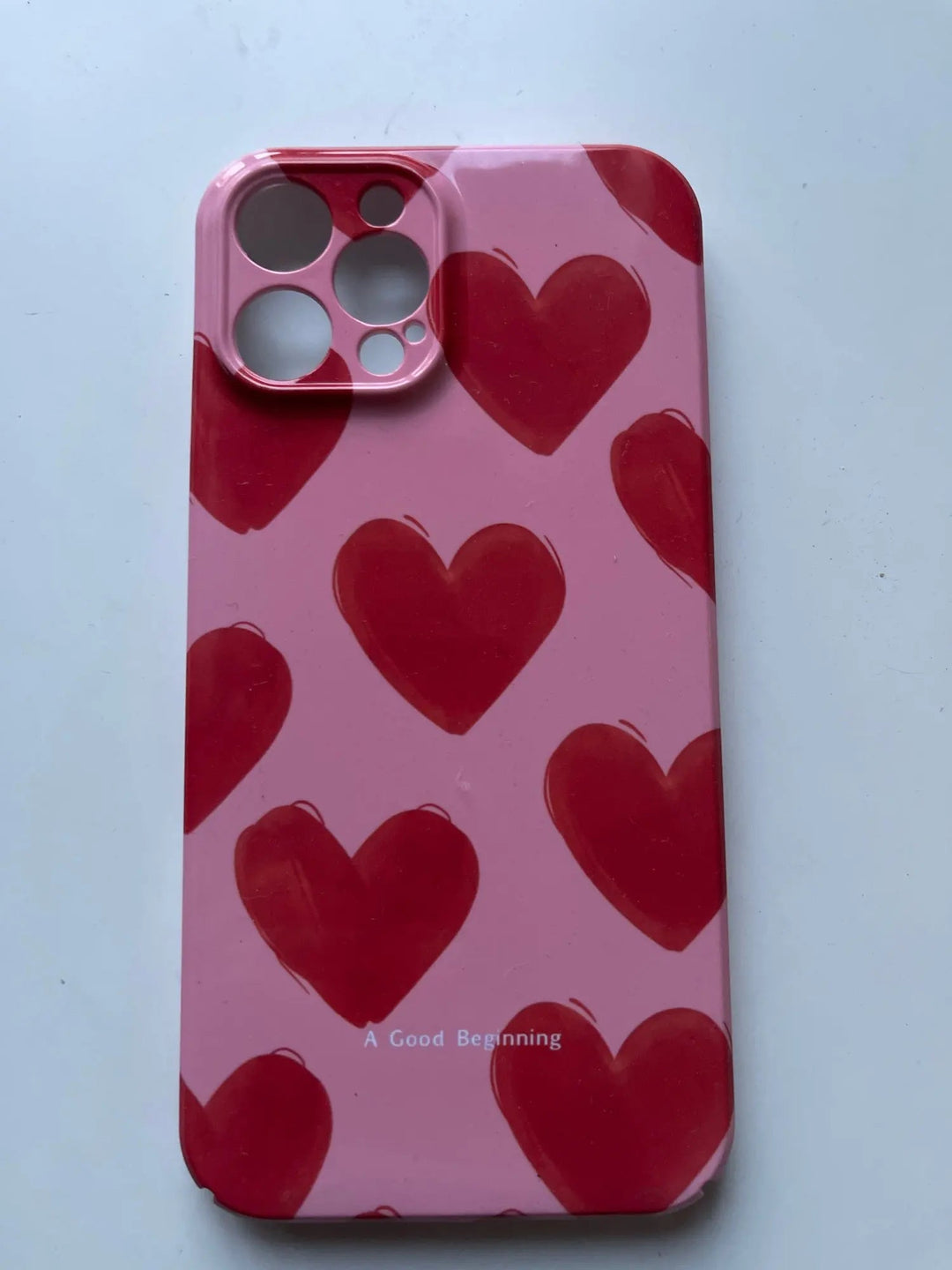 A sleek Couple Hearts for iPhone case in pink, featuring whimsical red heart patterns and the phrase "A Good Beginning" tastefully printed at the bottom.