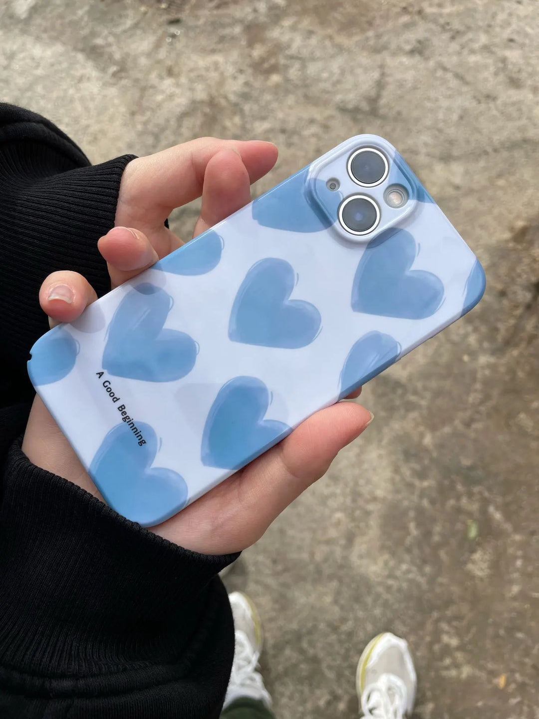 A person holding an iPhone encased in the Couple Hearts for iPhone - Acrylic, featuring a playful design with a white case adorned with blue heart patterns.