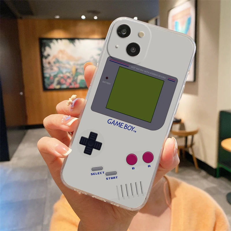 A hand holds an iPhone encased in the Gameboy Case For iPhone, styled to mimic a classic Game Boy with buttons and a screen. The blurred indoor decor, featuring a painting and a green chair in the background, enhances the retro gaming atmosphere.