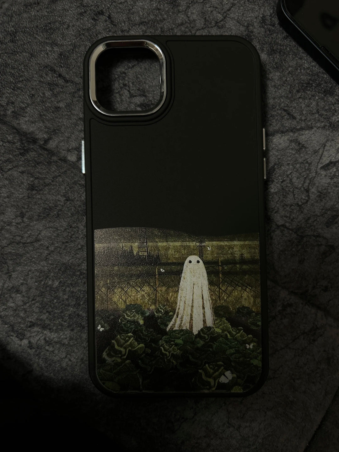 A black phone case with a white ghost standing in a field of green plants.