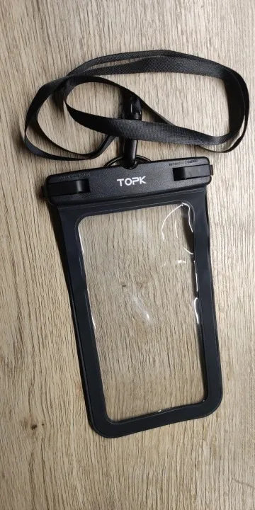 An IPX8 Waterproof Phone Pouch in black, showcasing a transparent window and equipped with a neck strap, is placed on a wooden surface. Perfect for outdoor activities, this pouch proudly displays the brand name "TOPK".