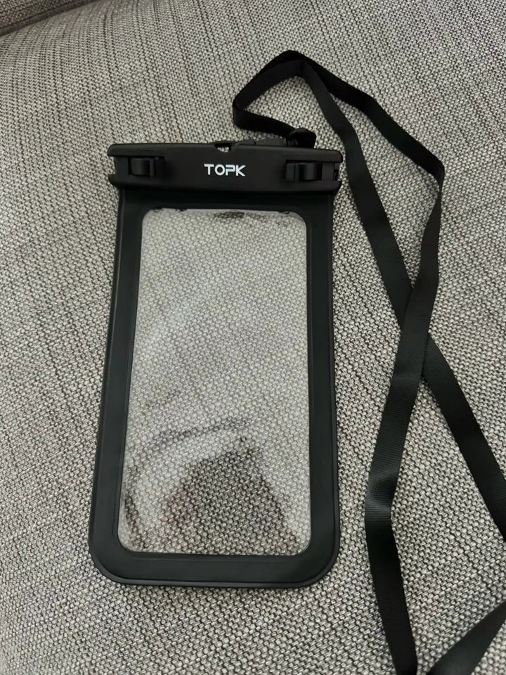 An IPX8 Waterproof Phone Pouch, featuring a black design and offering full protection against water, with clear front and back panels and secured by a black lanyard, rests on a textured gray fabric surface. Perfect for outdoor activities.