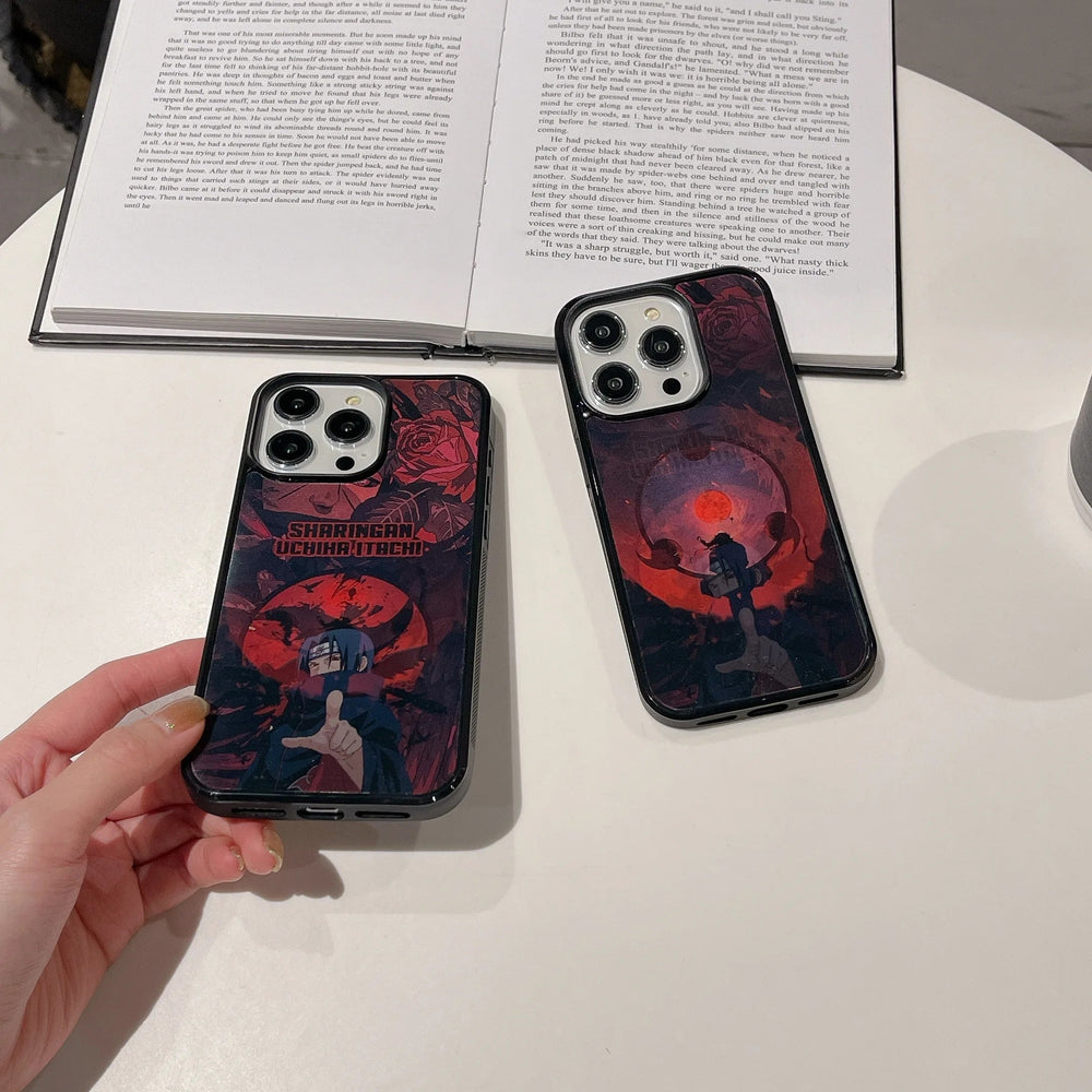 Two smartphones with matching "Itachi Angle Art" cases, featuring a dark-themed anime design showcasing Itachi from Naruto, are placed on a table, one held by a hand. An open book and a cup are also on the table. The Magsafe compatible cases add both style and convenience to your setup.