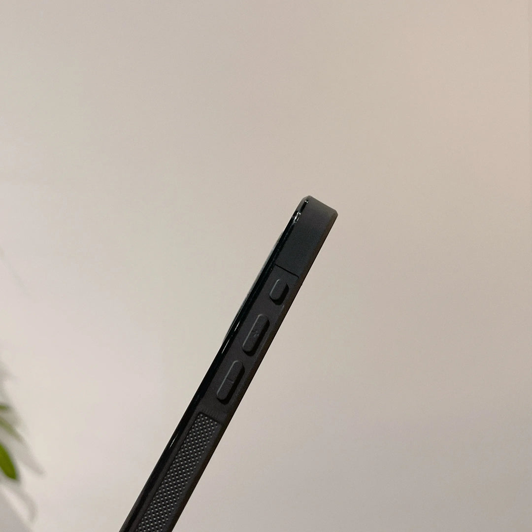 A close-up image of the Itachi Angle Art smartphone's side profile, showcasing volume control buttons and a textured grip detail with an Itachi-themed design. The blurred background with minimal detail highlights its sleek, MagSafe-compatible build.