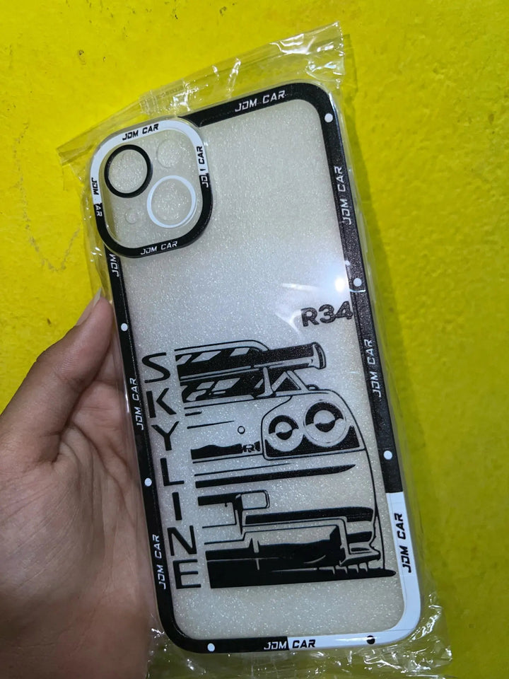 A hand holds a JDM Clear for iPhone silicone case, showcasing an illustration of a car with "SKYLINE R34" text. The anti-scratch case is in clear packaging against a vibrant yellow background, perfect for fans of JDM car designs.