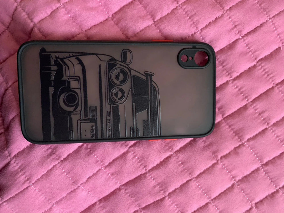 The JDM Frosted for iPhone, a protective phone case showcasing a black design with a car sketch on the back, lies on pink quilted fabric.