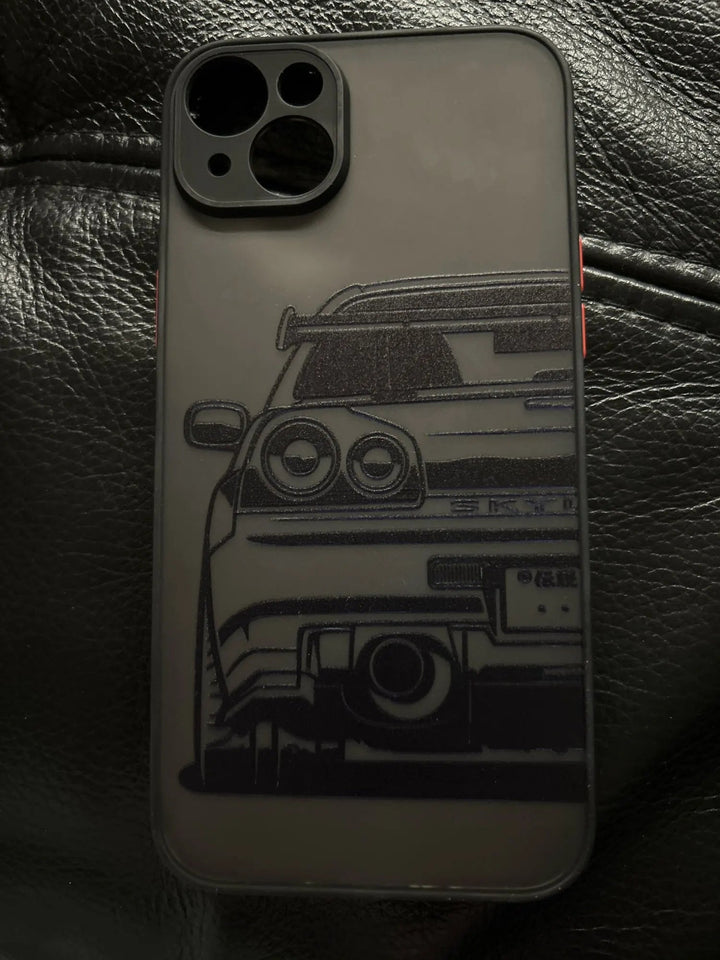 The JDM Frosted for iPhone, a TPU phone case with a translucent design showcasing the rear end of a sports car, is elegantly placed on a black leather surface.