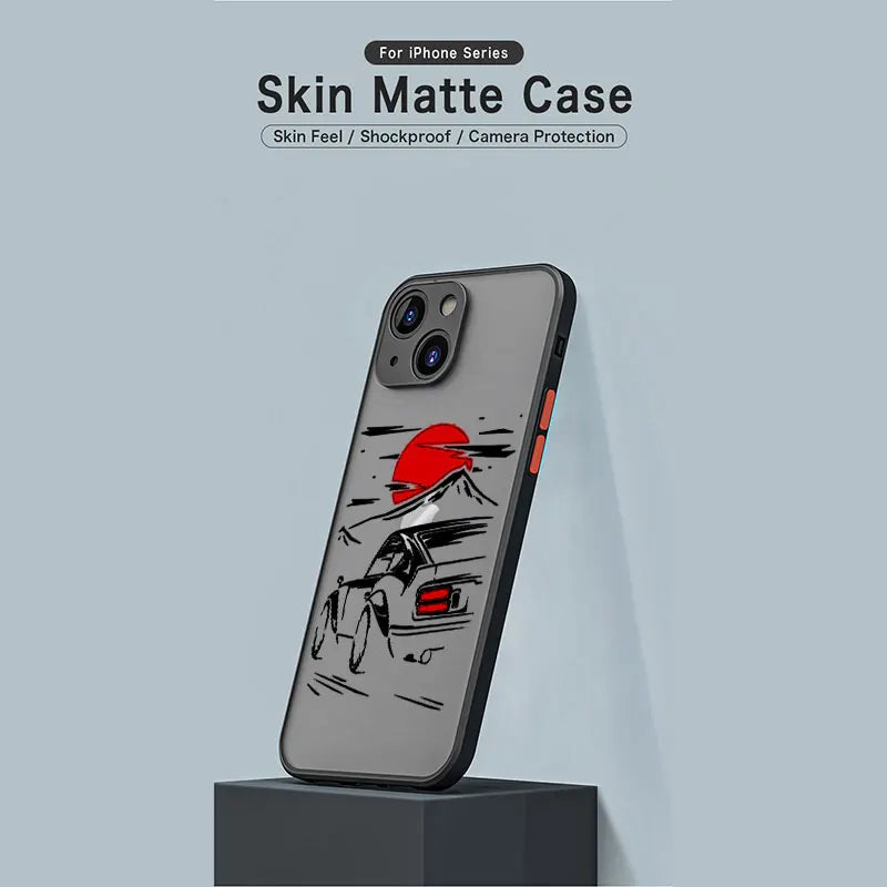 The JDM Sunset for iPhone case has a matte finish with a minimalist design of a red sun and mountains, inspired by JDM cars. This protective case features a skin-like feel, is shockproof, and offers camera protection.