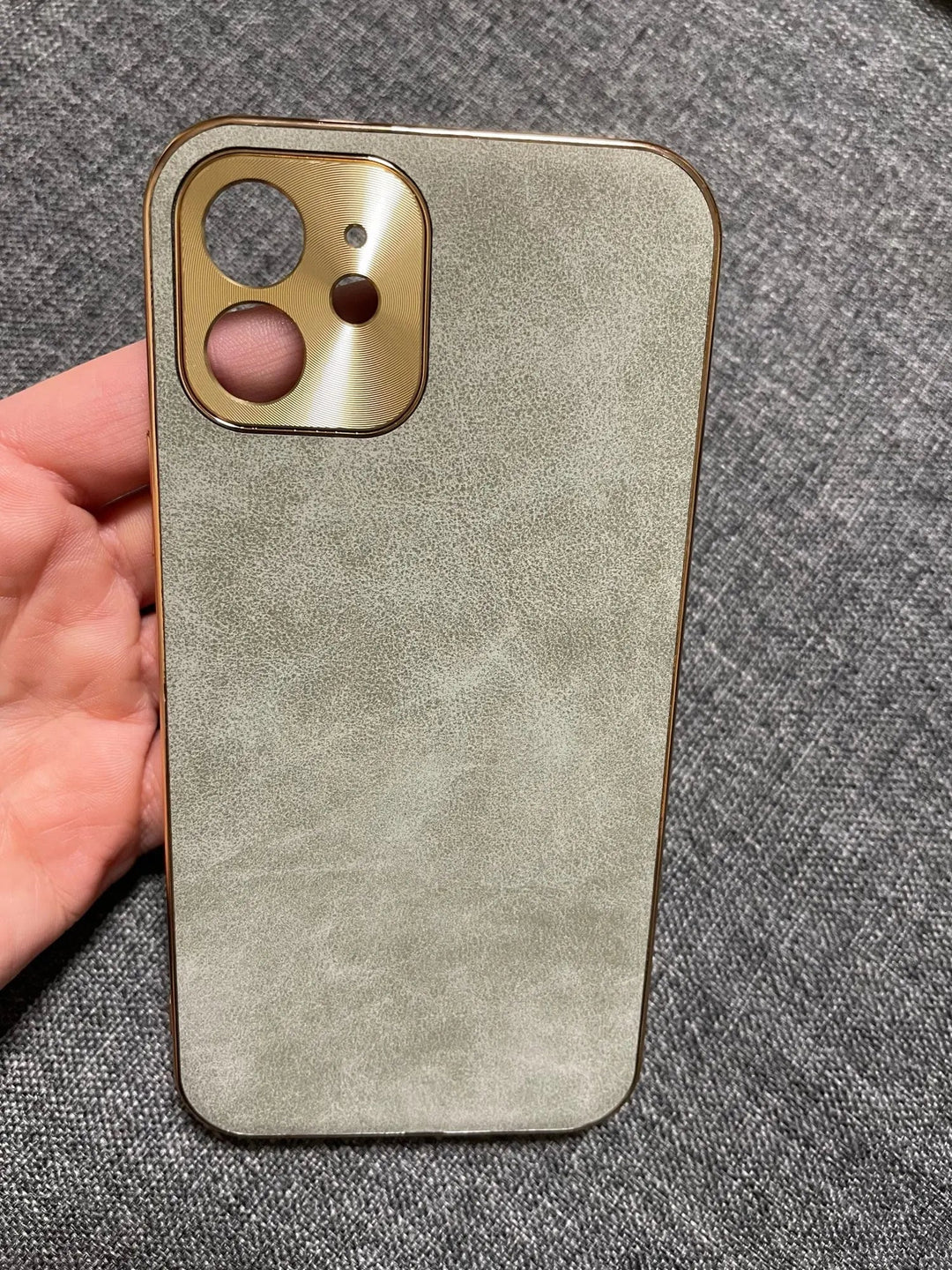 A person holding an iPhone with a textured, light-colored back, enhanced by the Lambskin Leather case featuring a gold camera cutout, on a dark fabric surface.