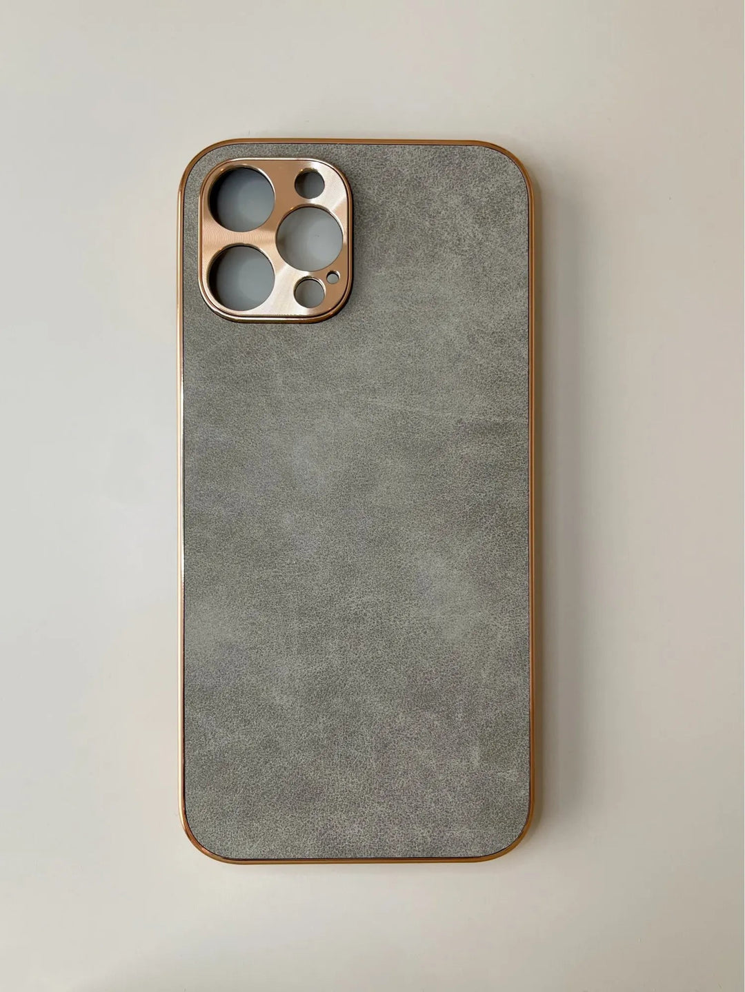 A grey smartphone with a metallic camera housing featuring three large circular openings and one small circular opening sits on a pale surface, complemented by a Lambskin Leather for iPhone case with a gold camera cutout.