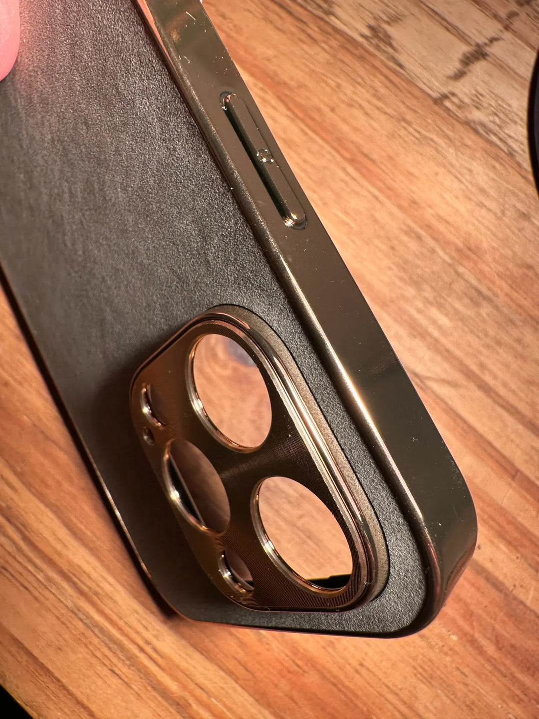 Close-up of an iPhone encased in Lambskin Leather, resting on a wooden surface, highlighting the side buttons and the gold camera cutout.