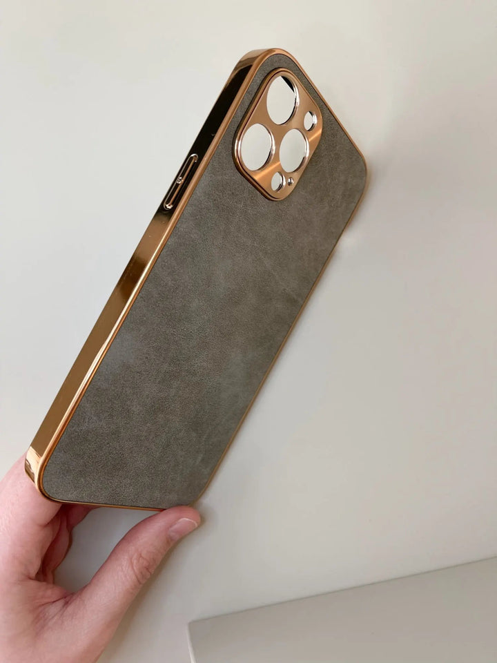 A hand holding a phone with the Lambskin Leather for iPhone case, featuring gold-colored edges and precise rear camera cutouts.