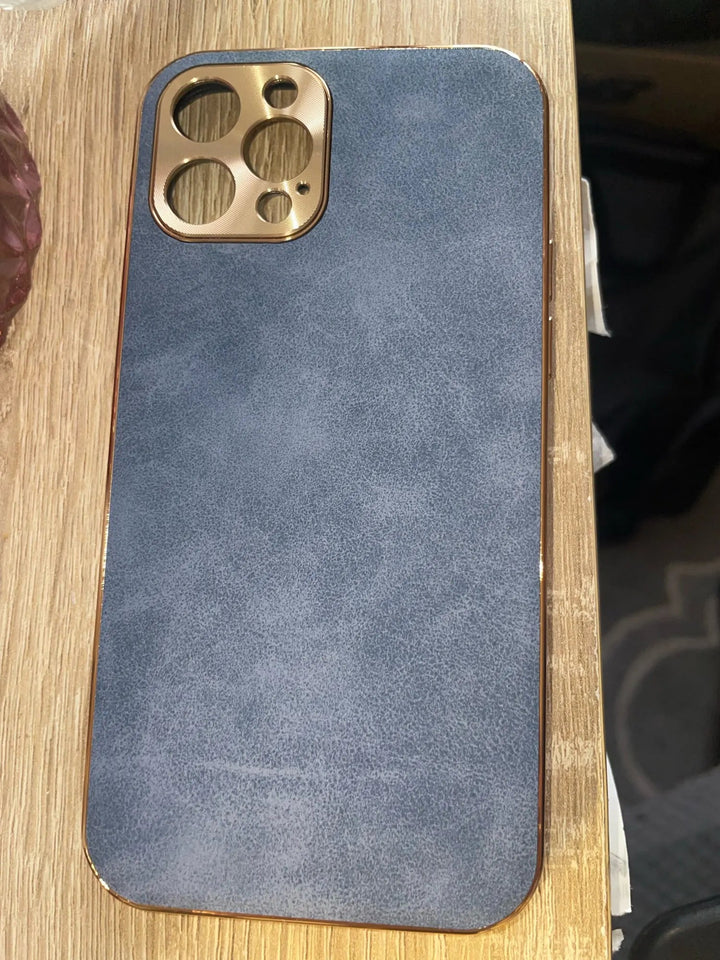 An iPhone encased in a premium Lambskin Leather for iPhone with a gold camera cutout rests on a wooden surface.