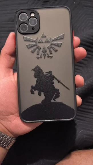 A hand holds a Legend of Zelda for iPhone case, showcasing a silhouetted knight on a rearing horse wielding a sword reminiscent of the Master Sword, with an emblem above.