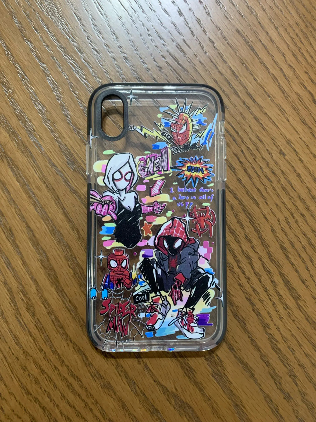 A transparent phone case with a colorful Spider-Verse design. It features characters like Miles Morales, Gwen Stacy, and other Spider-People