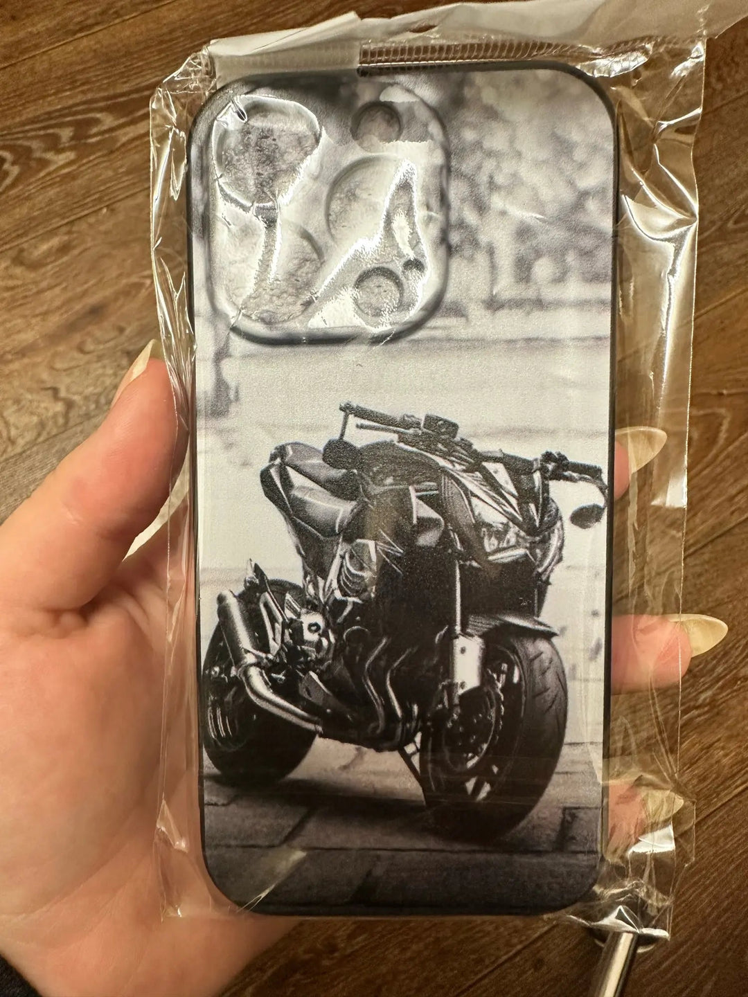 A hand holds a Motocross for iPhone, a lightweight, packaged phone case featuring a black and white image of a motocross design motorcycle with anti-scratch durability.