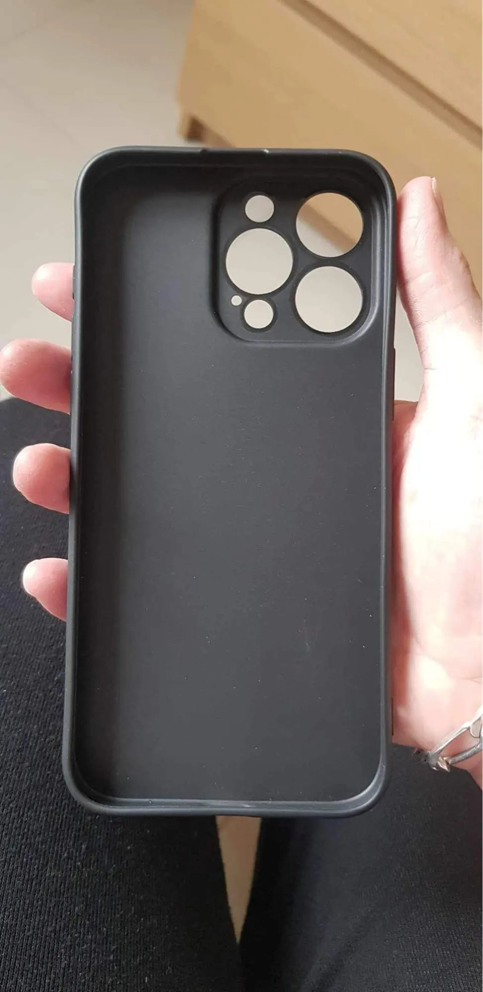 A person holding the Motocross for iPhone, a black, lightweight smartphone case featuring multiple camera cutouts designed specifically for a phone with a multi-lens camera system. The stylish motocross design also offers anti-scratch protection.