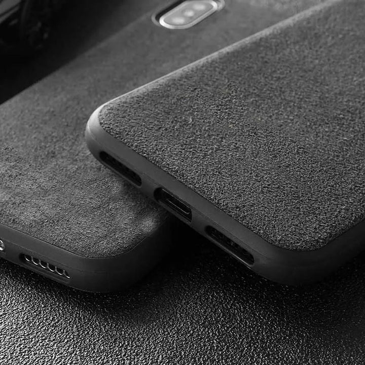 Close-up of two Nurburgring for iPhone black textured cases with visible cutouts for the camera, charging port, and speakers, lying on a dark surface. The cases feature the Nurburgring logo and are lined with Suede Microfiber for an elegant touch while offering anti-scratch protection.