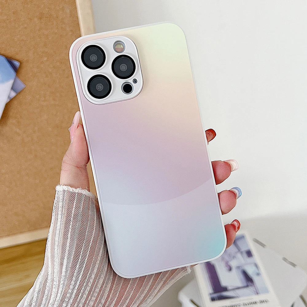 A hand holding an iPhone encased in the Ombre Glass Case, showcasing a triple-camera setup on the back. The person, with multi-colored nails and a mesh sleeve, ensures their phone remains sleek and stylish due to the case's anti-fingerprint and anti-scratch features.