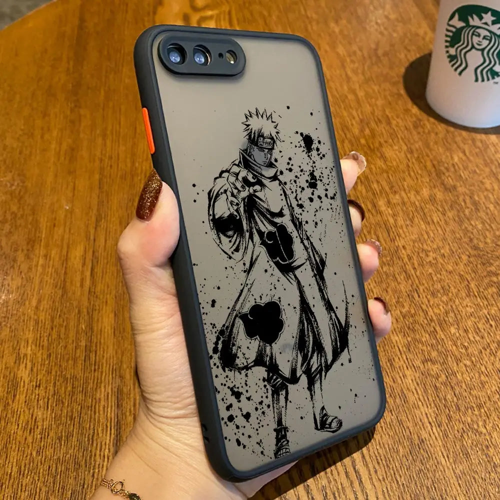 A hand holds a smartphone with the Pain Translucent anti-scratch case featuring the Akatsuki leader in a robe. There's a Starbucks cup on a wooden table in the background.