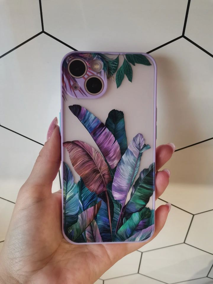 A close-up photo of a hand holding a frosted phone case with a vibrant tropical leaf design. The leaves are painted in shades of blue, green, and purple.