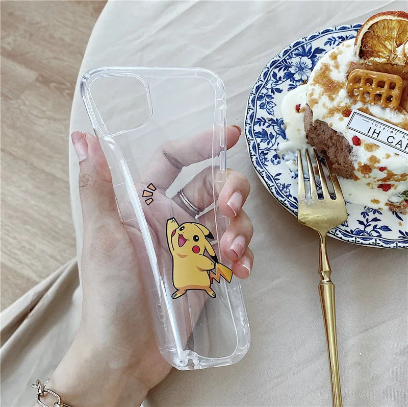 A hand holding a Pikachu Clear Case for iPhone with an anti-scratch design. A plate with dessert and a gold fork are on a table in the background.