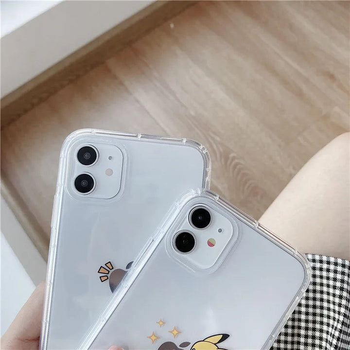 Two iPhones protected with Pikachu Clear Cases, each adorned with a decorative Pikachu design, are being held. The devices rest on a wooden surface, and part of a checkered fabric can be seen in the frame.