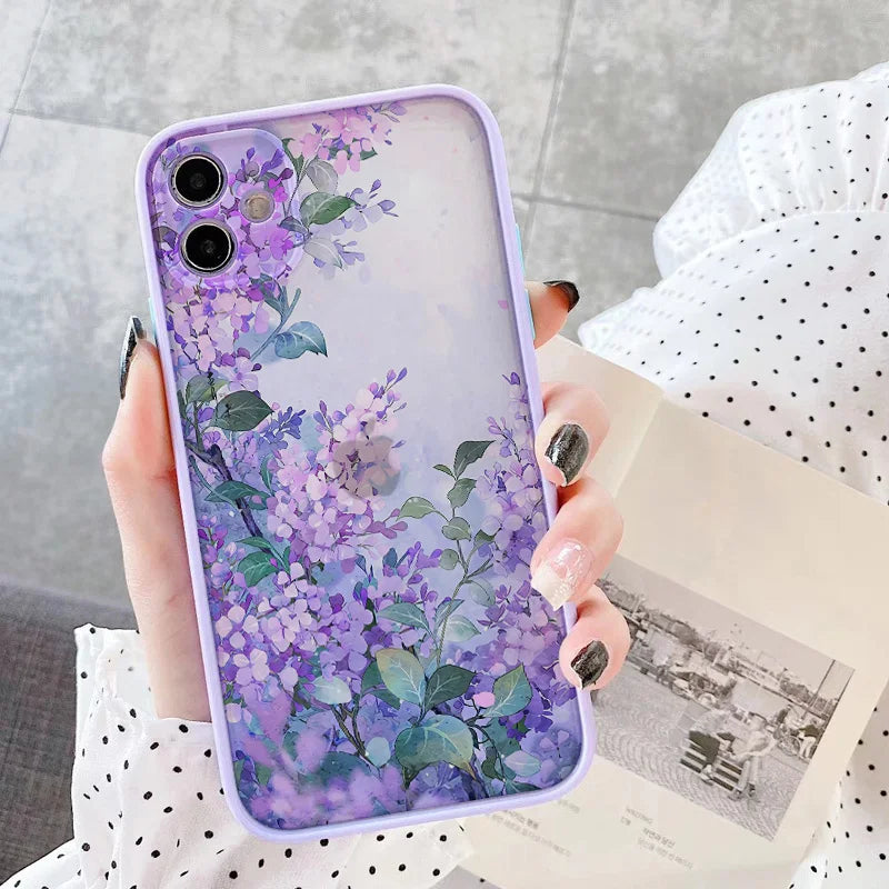 A close-up photo of a hand holding a frosted phone case with a watercolor painting of purple lilac flowers