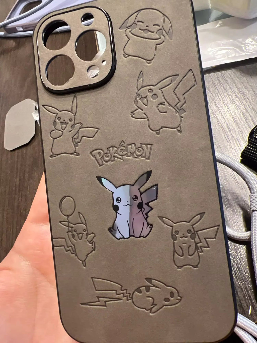 A hand holds the Retro Pikachu for iPhone case, which features multiple embossed Pikachu illustrations and the word "Pokémon." The silicone case also has a cutout of Pikachu in the center.