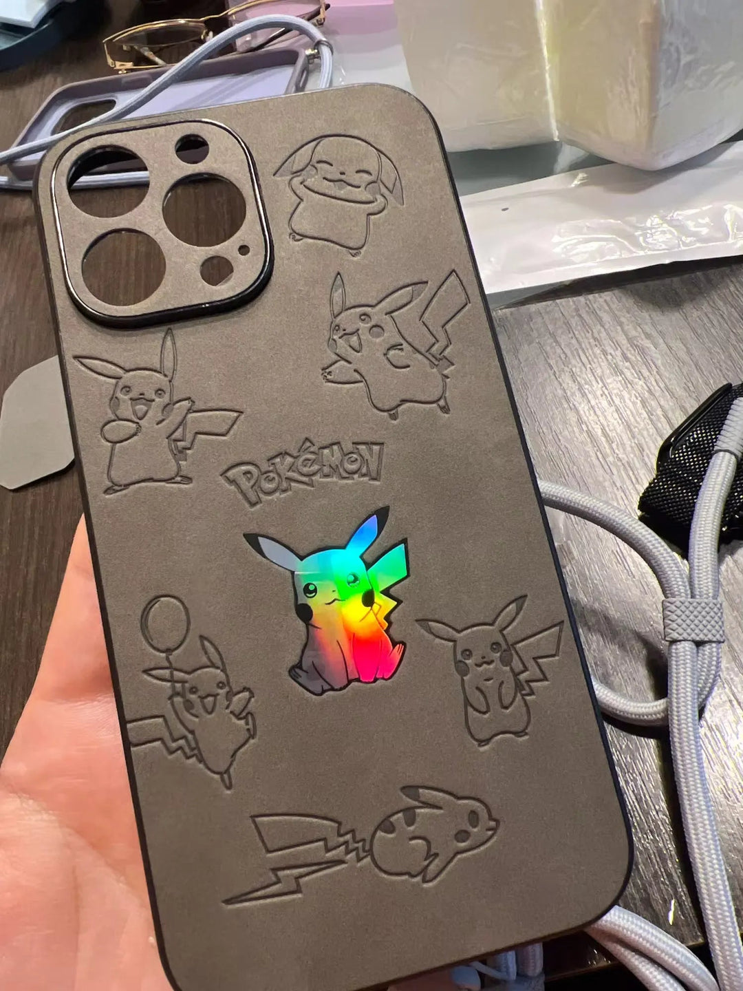 A hand holds the Retro Pikachu for iPhone, a silicone case showcasing embossed Pikachu illustrations and a rainbow-colored Pikachu cutout, complete with a phone camera hole.