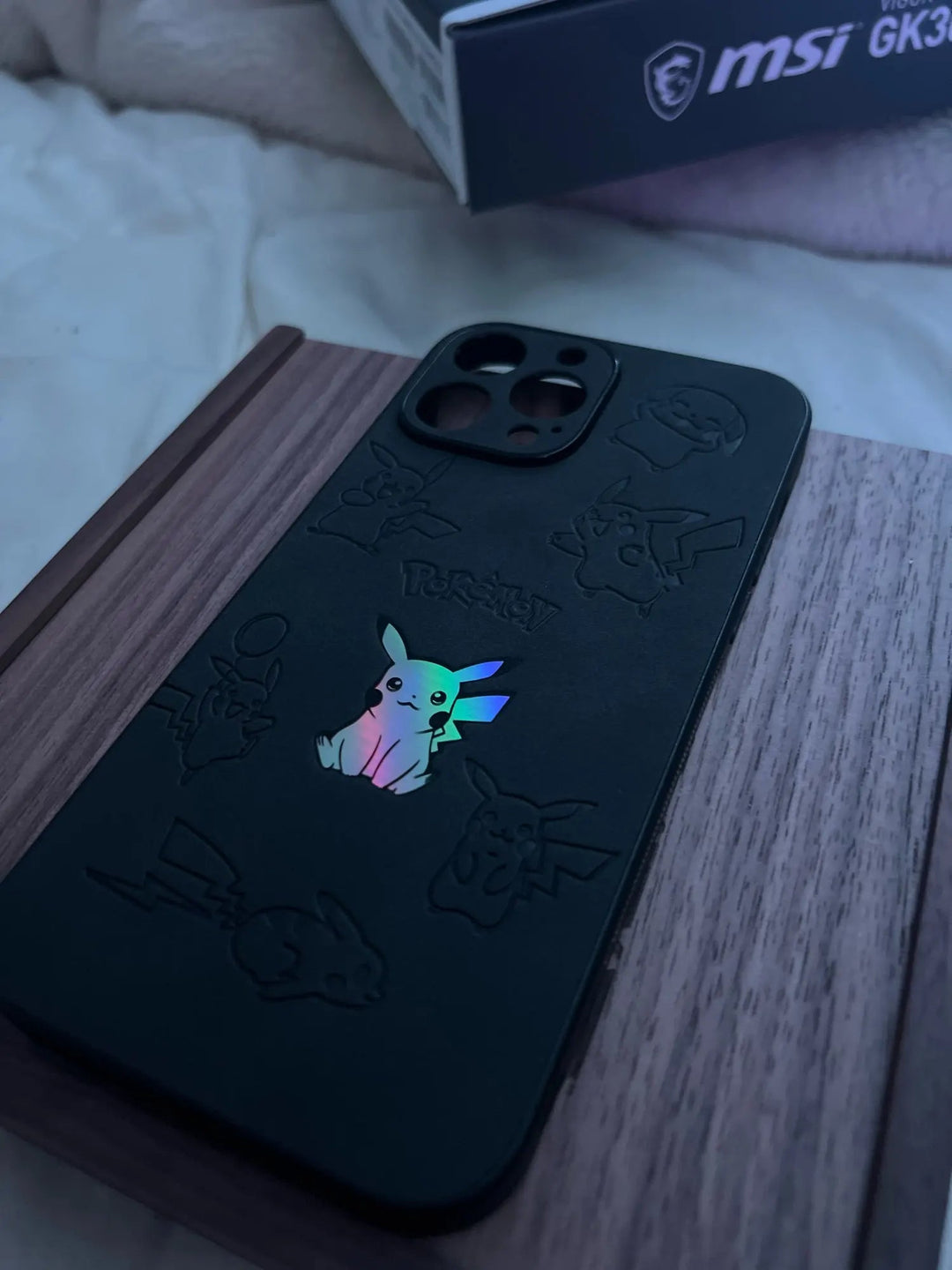 The "Retro Pikachu for iPhone" silicone case, featuring a glowing Pikachu design and retro-inspired Pikachu illustrations in black, is placed on a wooden surface.