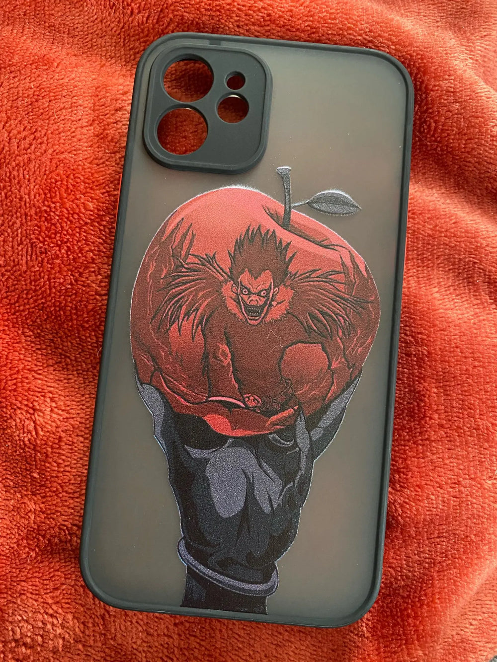 A frosted phone case with a matte finish and a red apple design featuring Ryuk, the Shinigami, from Death Note