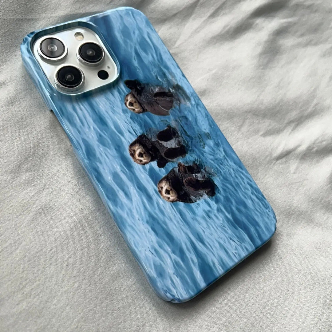 The Sea Otter Case for iPhone - Acrylic features an image of three otters swimming in blue water, making it the perfect accessory for ocean enthusiasts and animal lovers.