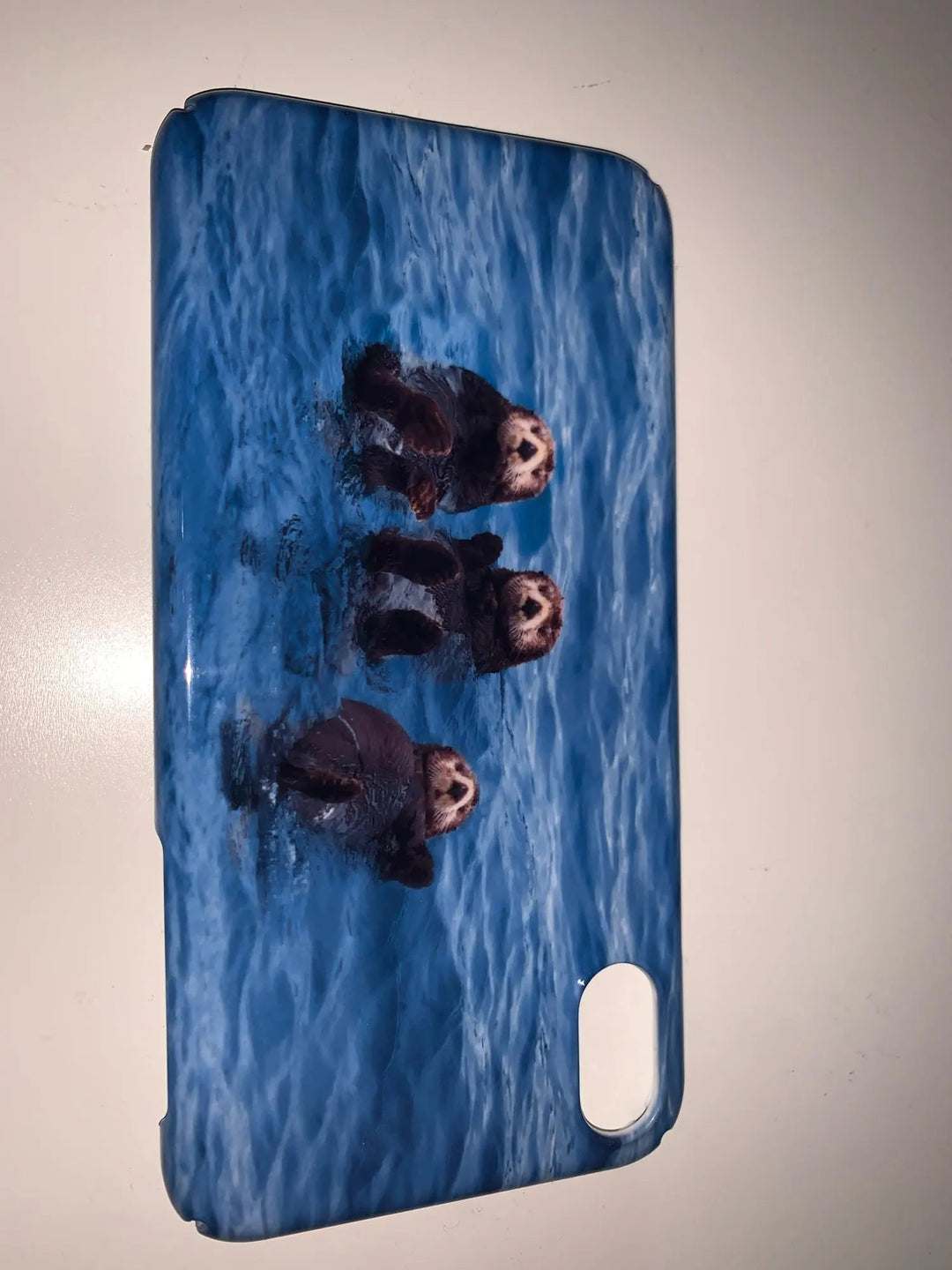 The Sea Otter Case for iPhone - Acrylic showcases a captivating photograph of three otters floating in the water, with a serene blue ocean backdrop—ideal for animal lovers and ocean enthusiasts.