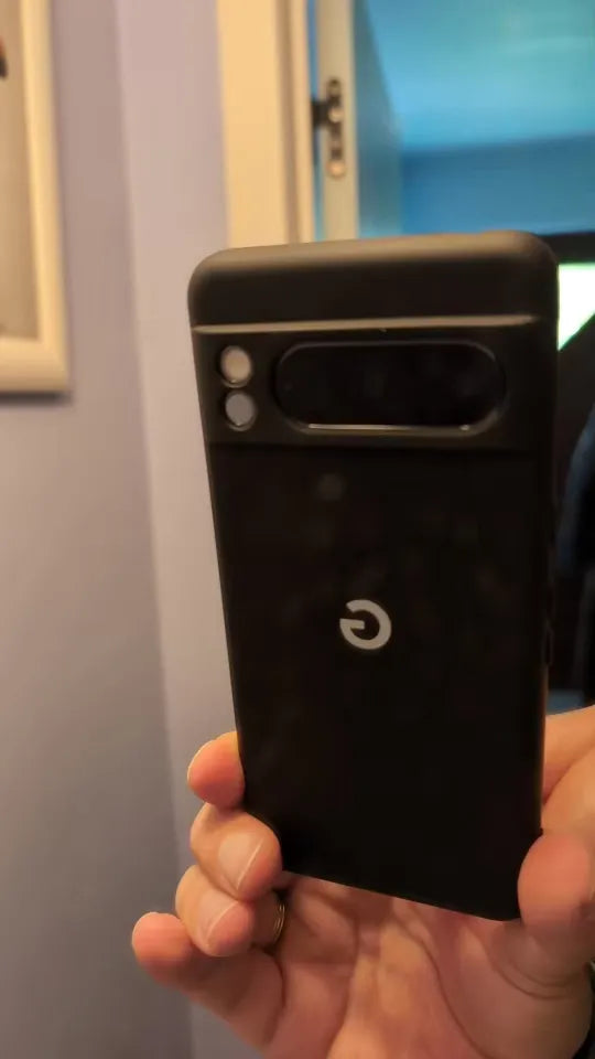 Close-up of a person holding a black Google Pixel smartphone with a distinctive camera module and a "G" logo on the back, encased in the sleek Silicone Case for Google Pixel that offers maximum protection and anti-scratch features, all reflected in front of a mirror.