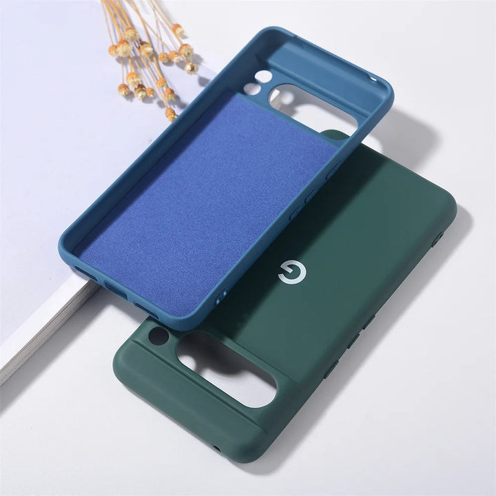 Two Silicone Cases for Google Pixel on a white surface; one is blue with a purple interior, and the other is forest green. Both offer maximum protection, are anti-scratch, and compatible with smartphones featuring dual camera cutouts.