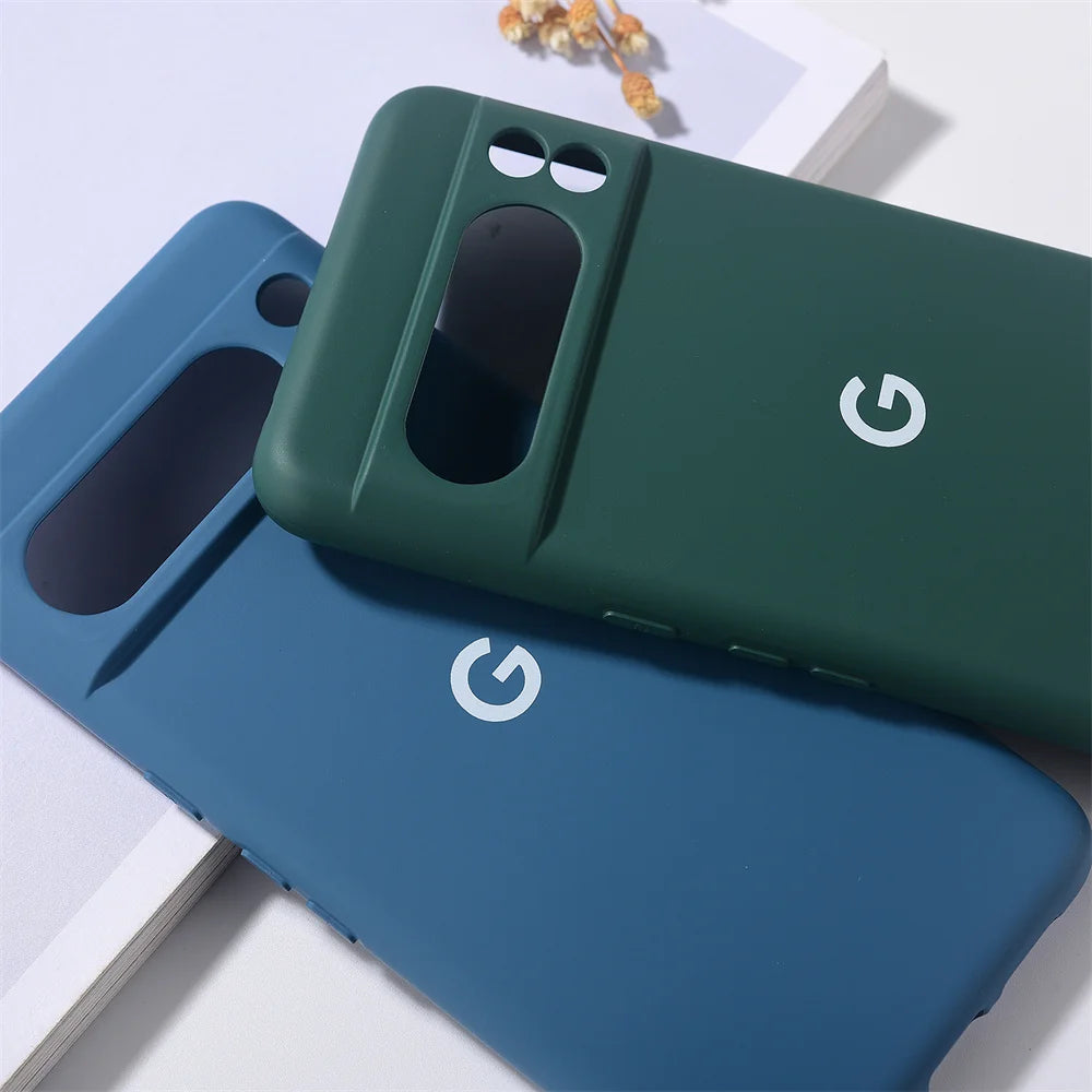 Two Silicone Cases For Google Pixel, one blue and one green, lie on a white surface. These slim-fit cases offer maximum protection with precise cutouts for cameras and fingerprint sensors, showcasing a 'G' logo in the center.