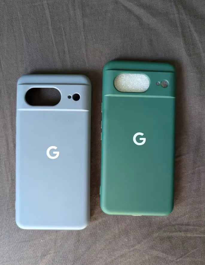 Two sleek Silicone Cases for Google Pixel—one in gray and the other in green—each adorned with a contemporary "G" logo. Laid side by side on a dark fabric surface, they provide robust protection and feature an anti-scratch design.