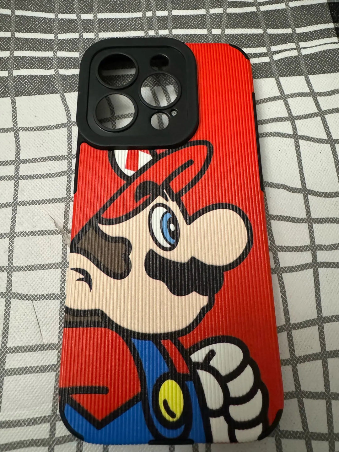 The Super Mario for iPhone smartphone comes with a durable, hard plastic case adorned in vibrant red, blue, and yellow. It features the iconic cartoon character with a mustache and hat, set against a stylish checkered backdrop.