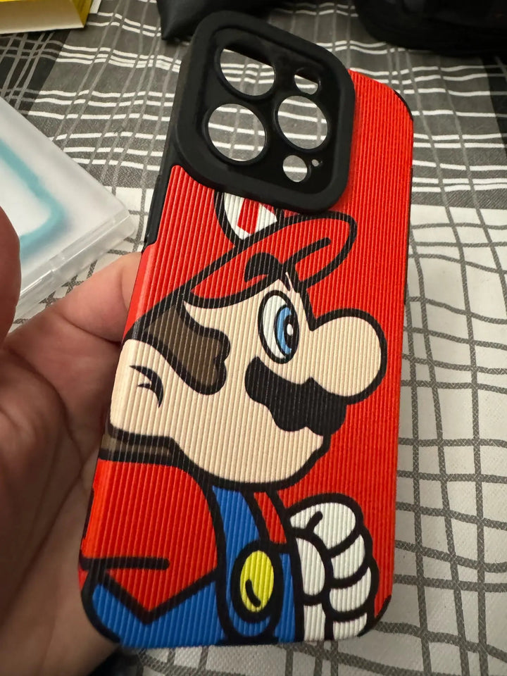 A hand is holding the Super Mario for iPhone protective case, which features a close-up image of the animated character with a red hat and mustache against a checkered tablecloth background. The phone case is made of durable hard plastic.