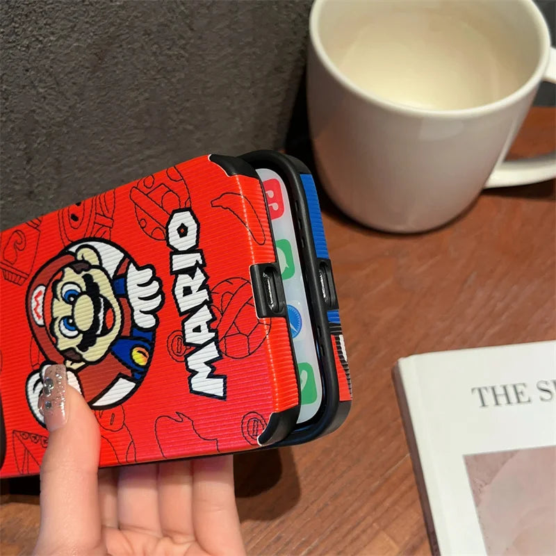 A smartphone in a Super Mario for iPhone case is being held next to a white mug and an open book on a wooden surface.