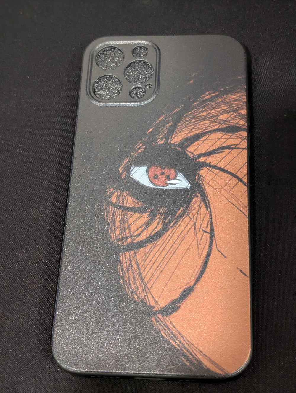 The Tobi Mask for iPhone showcases an eye-catching black and orange anime-style eye design on its back cover, enhanced by a triple-camera setup and wrapped in a sleek TPU case with a slim profile.